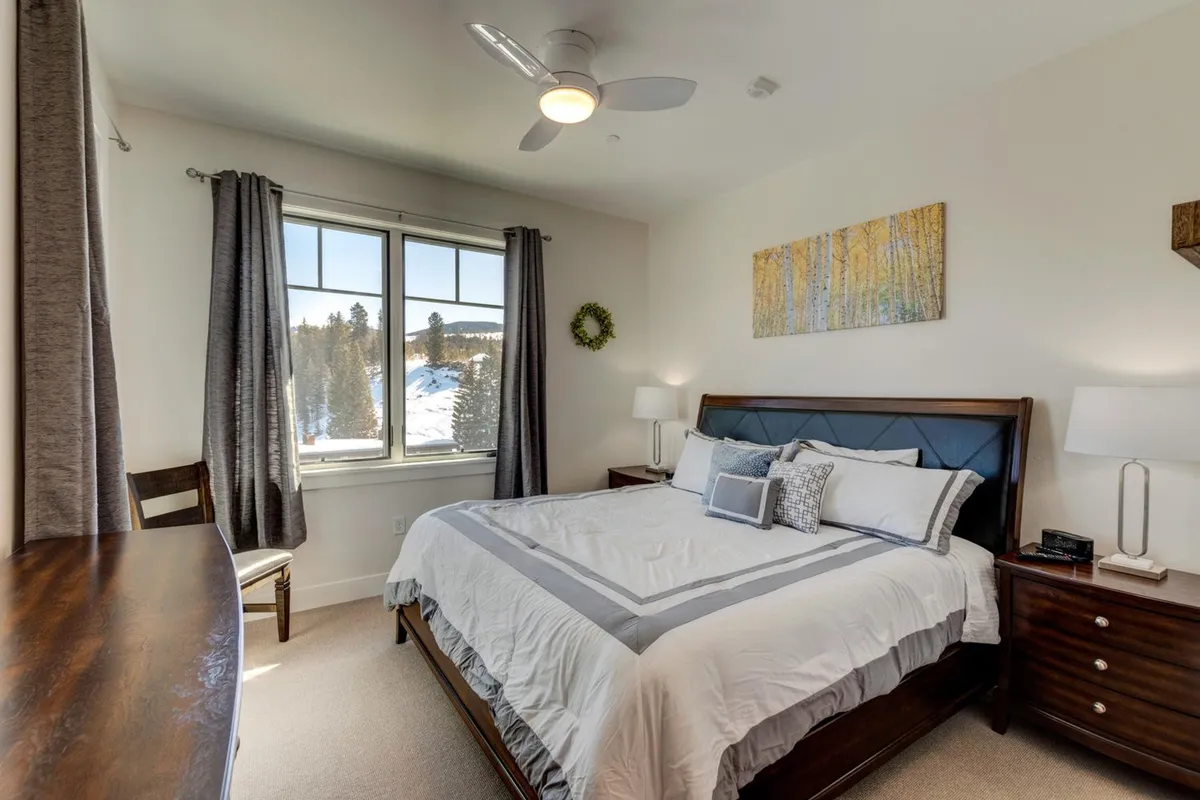 A serene bedroom with a plush bed, cozy window view, tasteful artwork on the wall, nightstands with lamps, and an inviting chair, radiating tranquility and comfort.