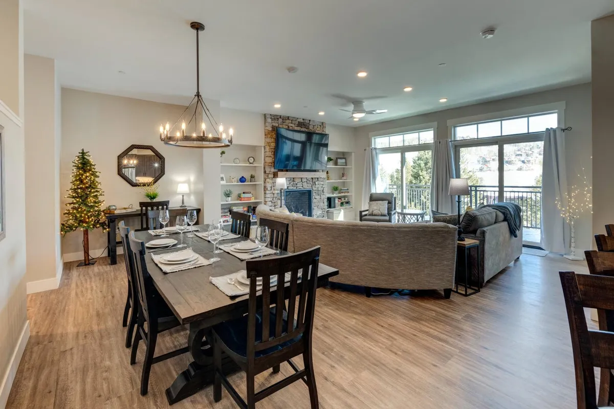 A broad view encompassing a dining table set for a meal, a decorated Christmas tree, a living room seating area, and a fireplace with a TV above. The inviting scene suggests togetherness, warmth, and special occasions.