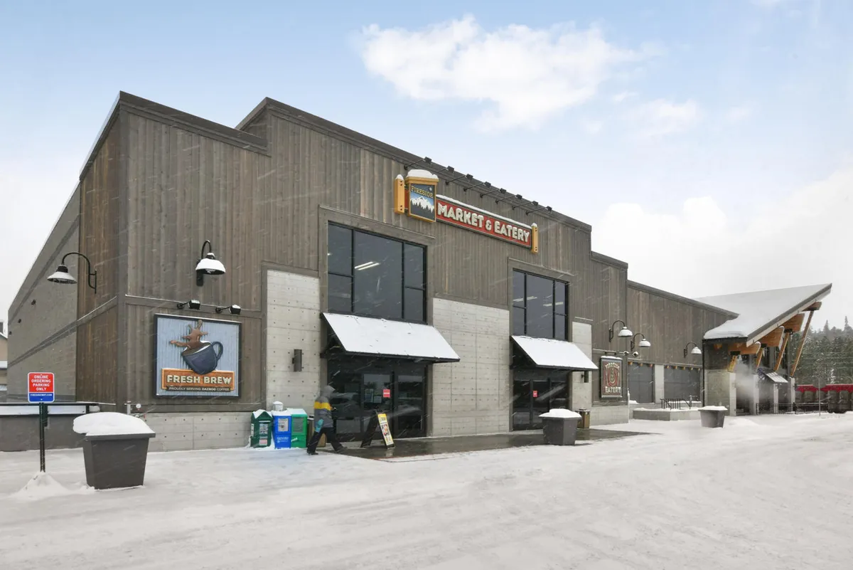 The image showcases the entrance to Fireside Market & Eatery, featuring distinctive signage, awnings, and a snow-covered ground, creating a warm and community-focused atmosphere. There are people nearby, suggesting activity regardless of season.