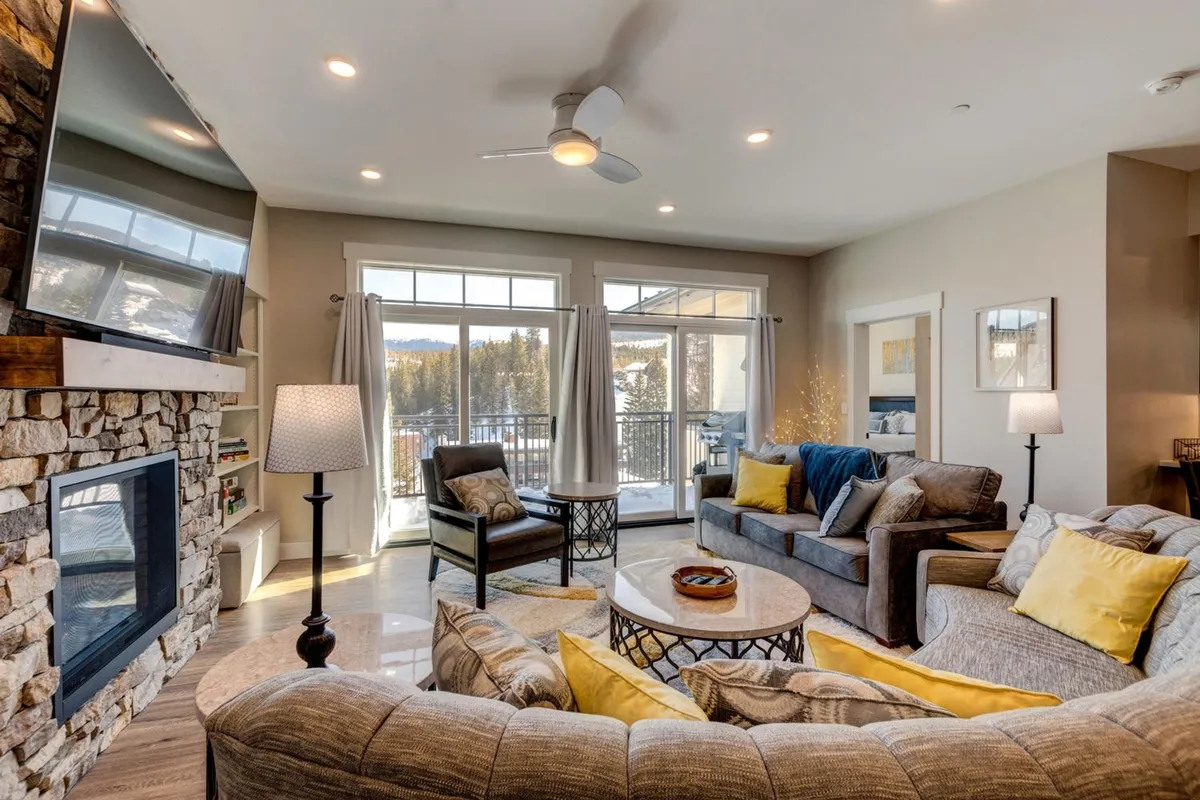 A cozy living room with a fireplace, large windows letting in natural light, ample comfortable seating, and a central coffee table. The layout encourages group interaction, relaxation, and allows for activities like board games or movie nights.