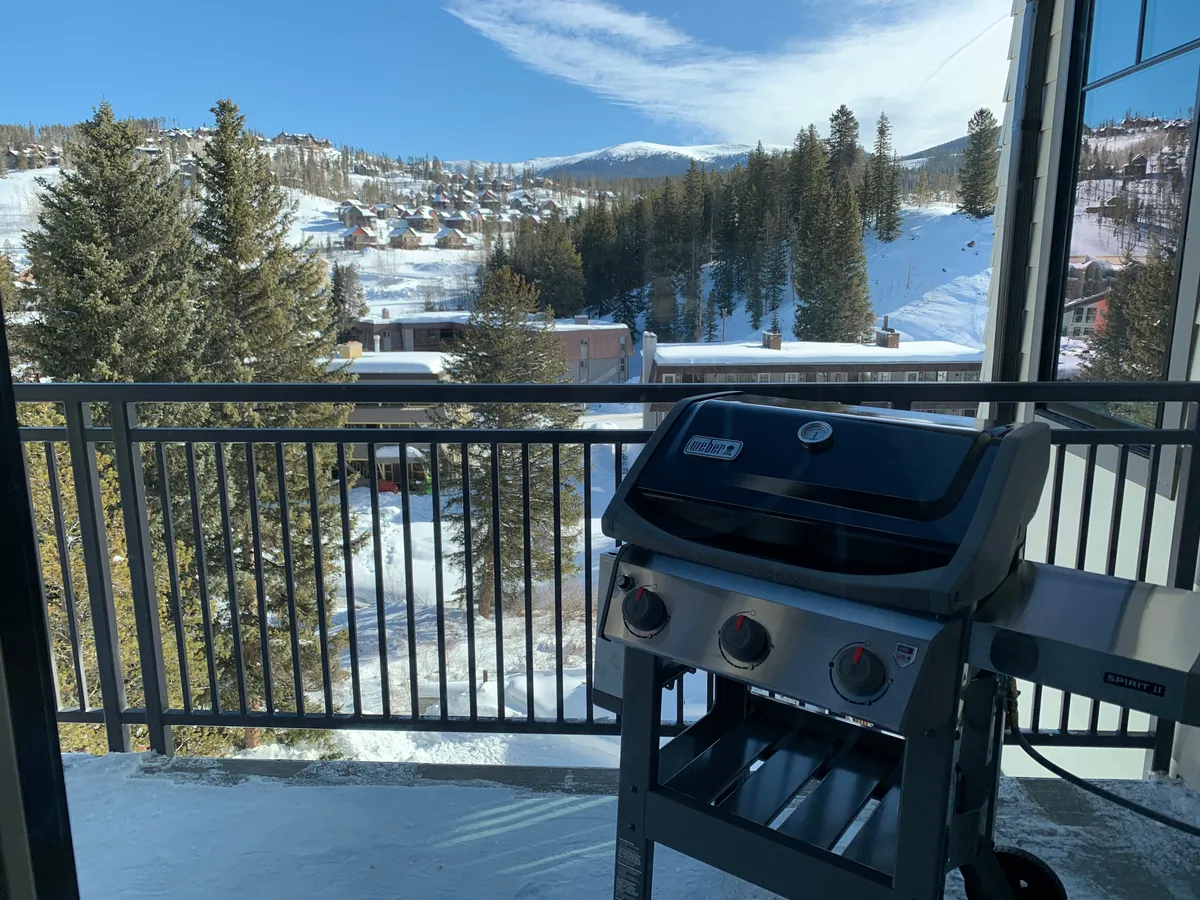 A balcony set against a snow-covered landscape, featuring a grill and mountain views. The scene suggests cozy moments like barbecuing or sipping hot drinks while enjoying the seasonal changes of the Colorado outdoors.